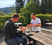 Zwei M&auml;nner sitzen drau&szlig;en an einer Holzgarnitur und vespern 